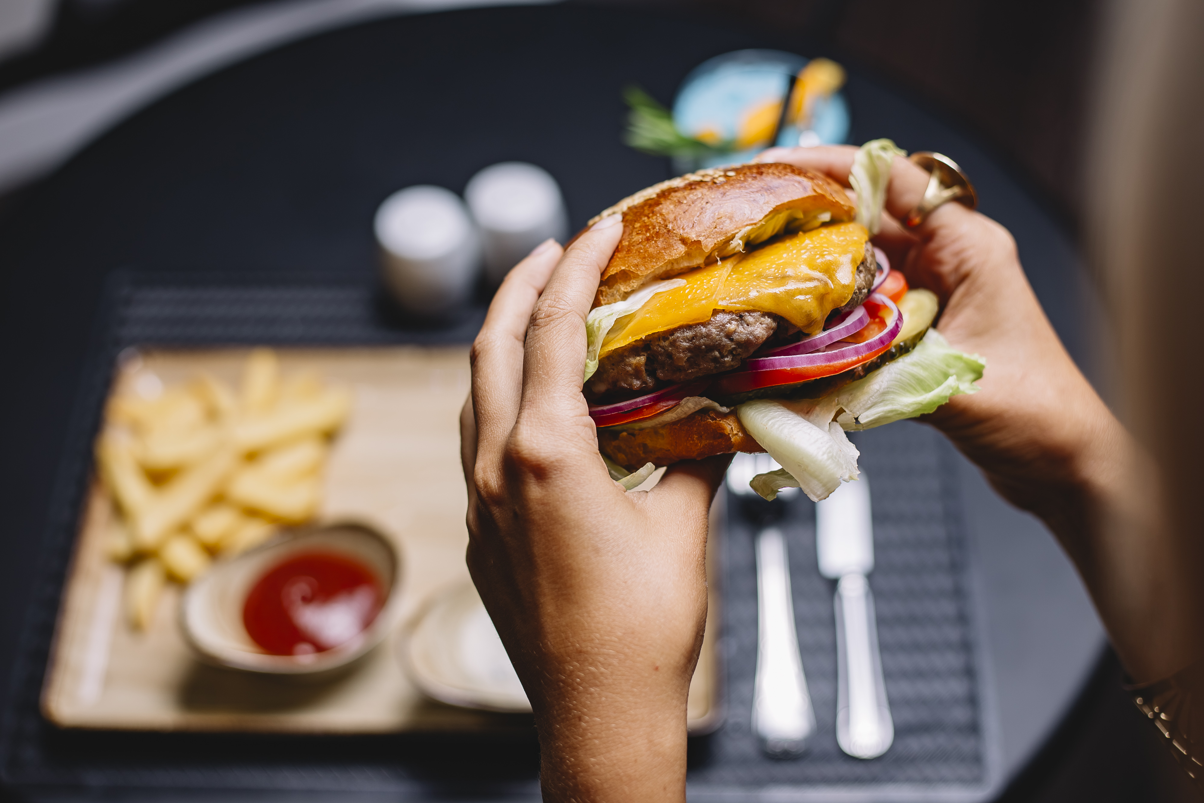 woman holds beef burger with lettuce tomato red onion and cheddar cheese